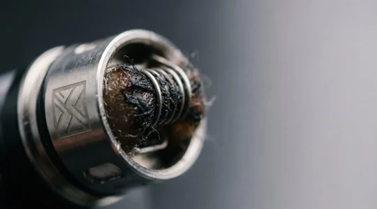 Close-up of a vape coil showing burnt cotton wick with vapor in a clean studio setting