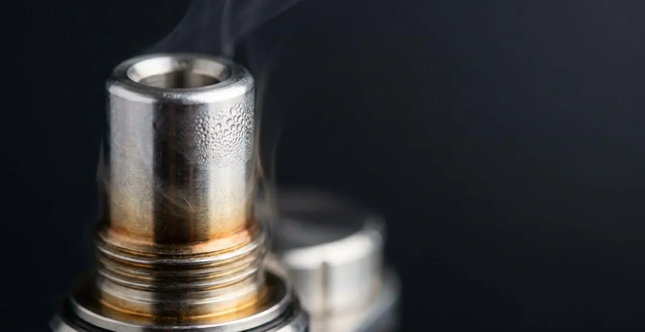 Close-up view of heated metal drip tip with thermal gradient and vapor condensation droplets in moody lighting